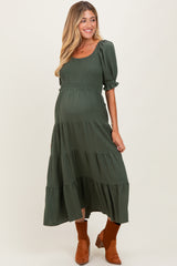 woman wearing a dark green maternity maxi dress with smocked bodice and tiered skirt, showing a baby bump
