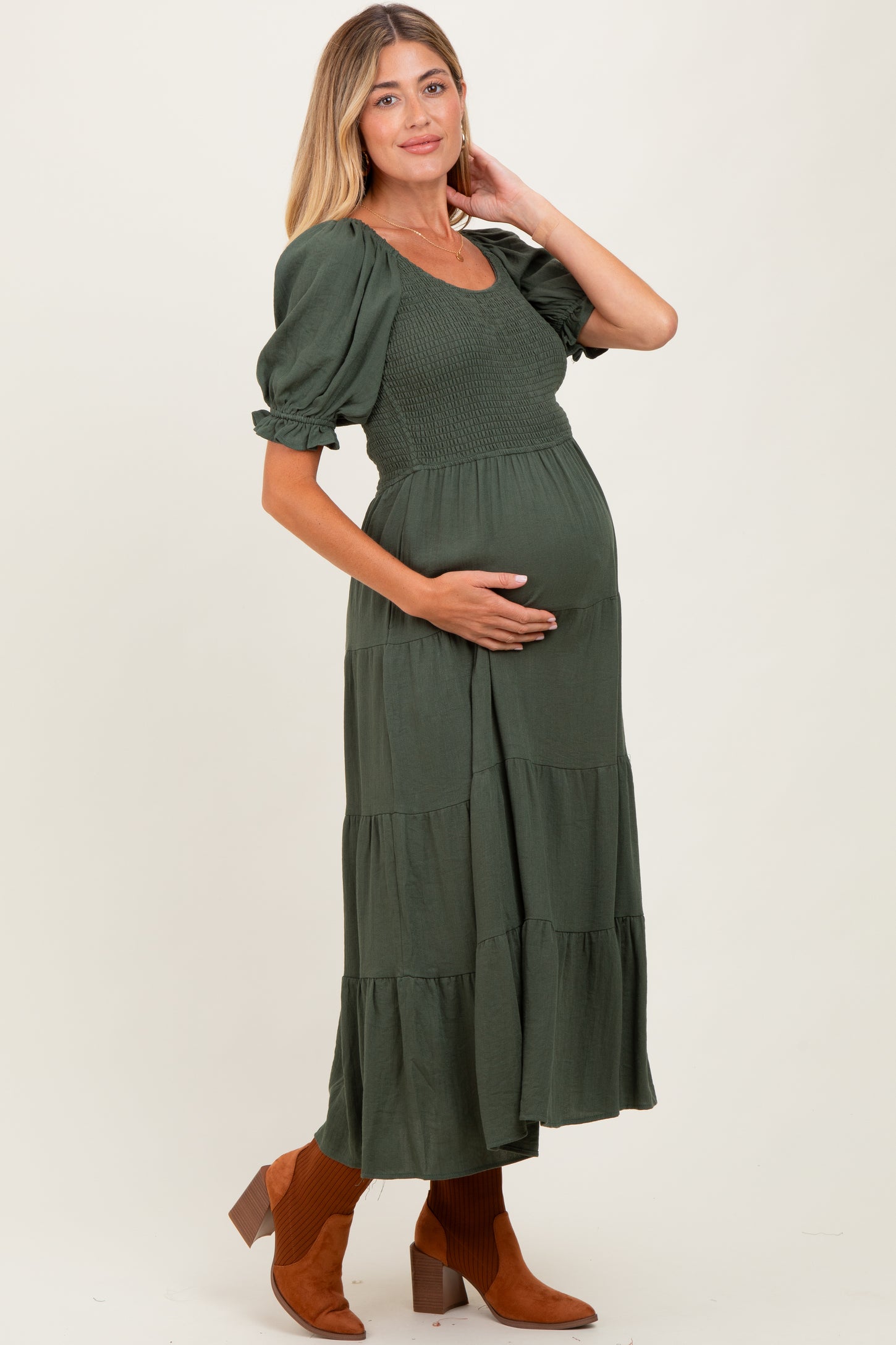 woman wearing a dark green maternity dress with puff sleeves and tiered skirt, cradling her baby bump
