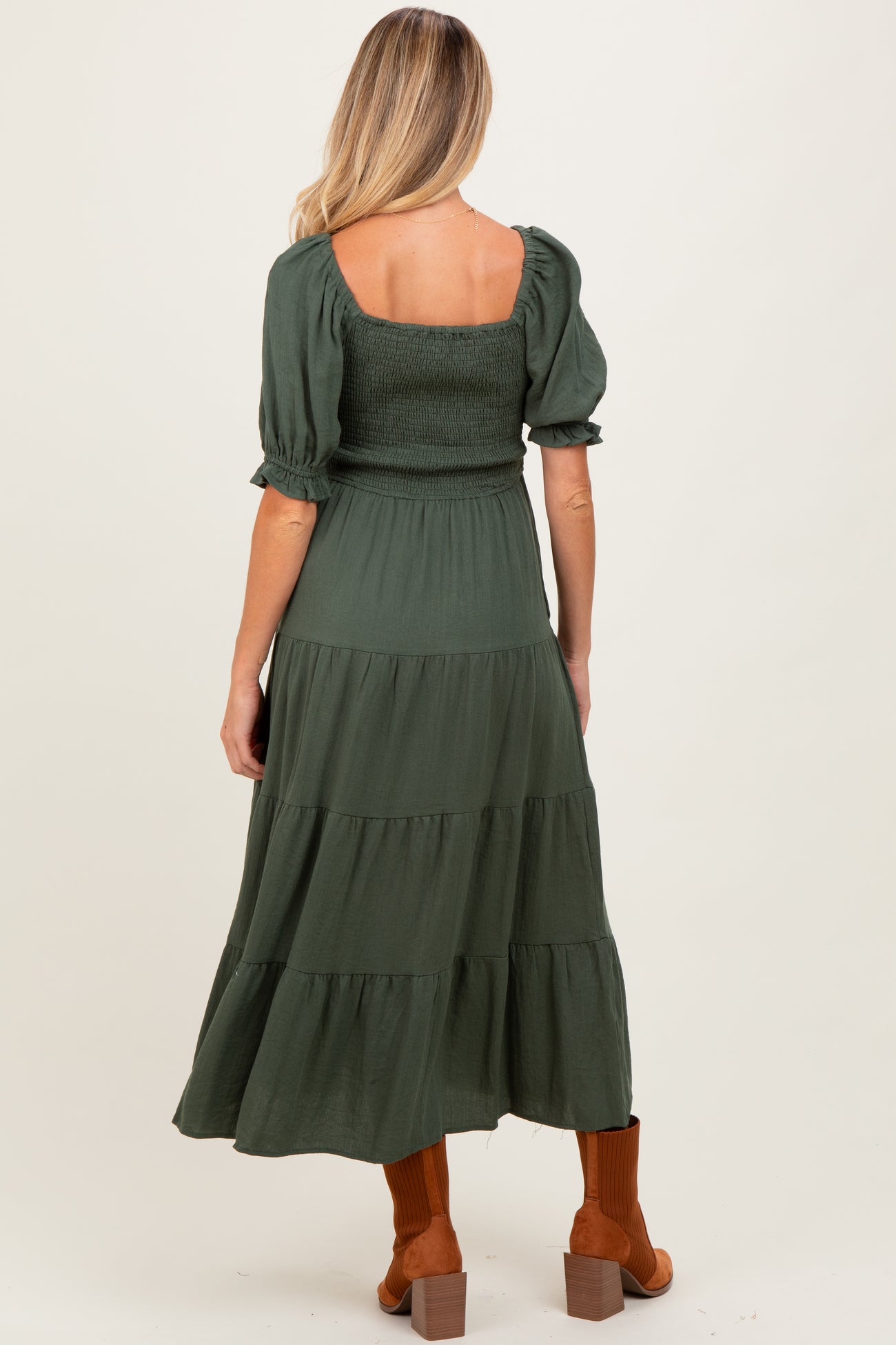 woman wearing a dark green maternity dress with puffed sleeves and a tiered skirt, showcasing baby bump from the back