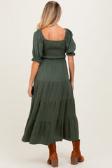 woman wearing a dark green maternity dress with puffed sleeves and a tiered skirt, showcasing baby bump from the back