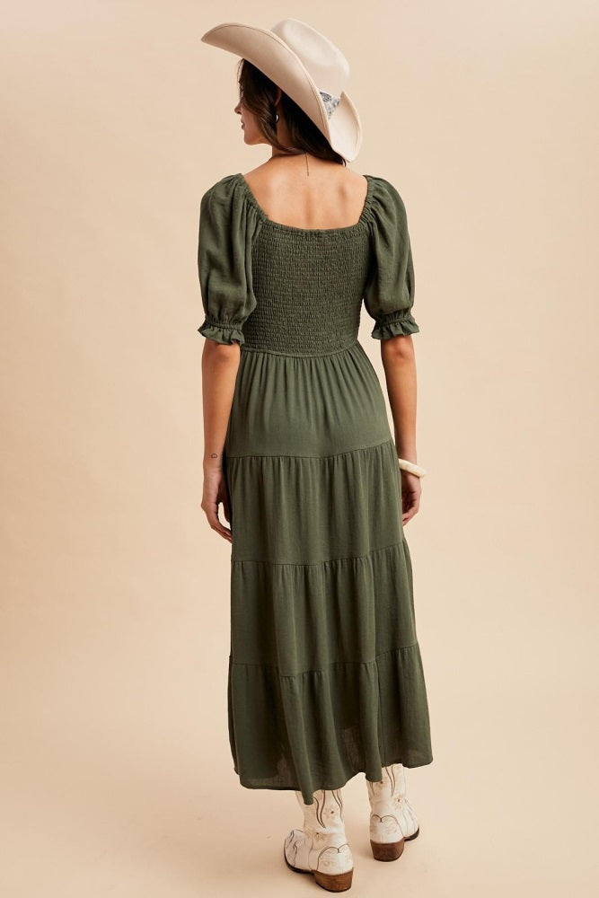 woman wearing a green tiered maxi dress with puff sleeves and a smocked bodice, seen from the back, paired with a cowboy hat