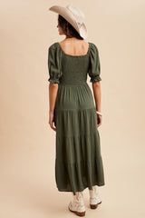 woman wearing a green tiered maxi dress with puff sleeves and a smocked bodice, seen from the back, paired with a cowboy hat