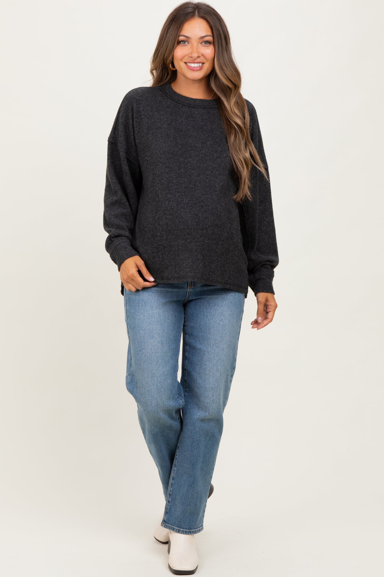 woman wearing a dark grey maternity sweater and light blue jeans, with a visible baby bump