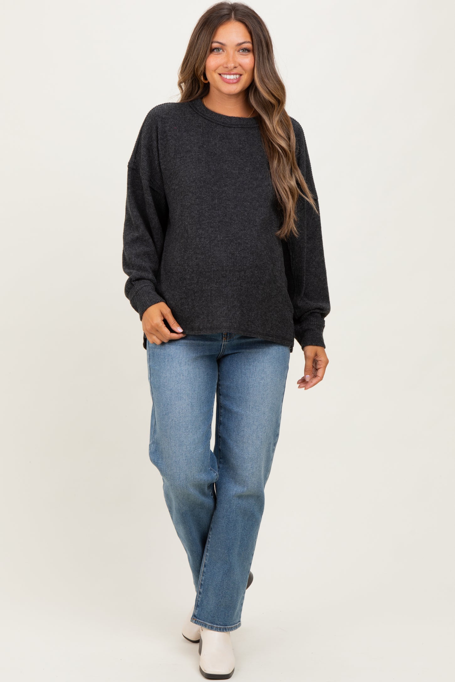 woman wearing a dark grey maternity sweater and light blue jeans, with a visible baby bump