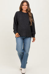 woman wearing a dark grey maternity sweater and light blue jeans, with a visible baby bump