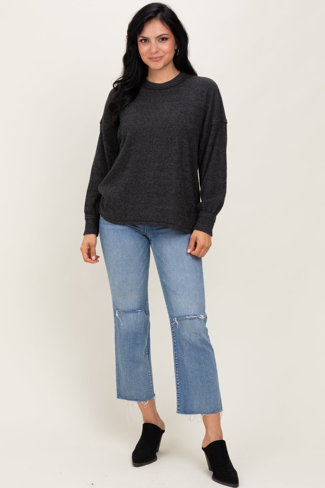 woman wearing a dark gray oversized sweater with long sleeves and distressed light wash denim jeans