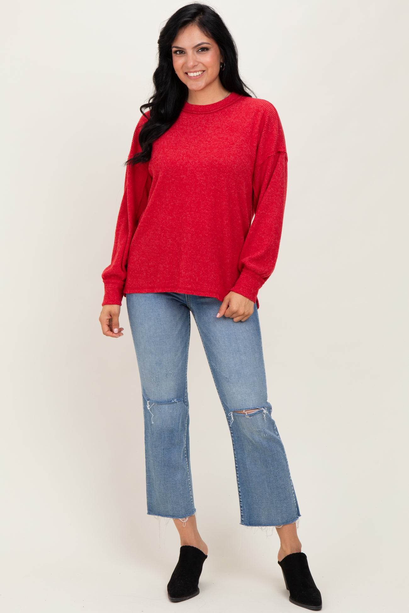 woman wearing a red oversized sweater and distressed cropped jeans, standing and smiling