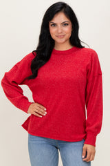 woman wearing a red relaxed fit long sleeve sweater with a textured fabric and side slits, paired with blue jeans