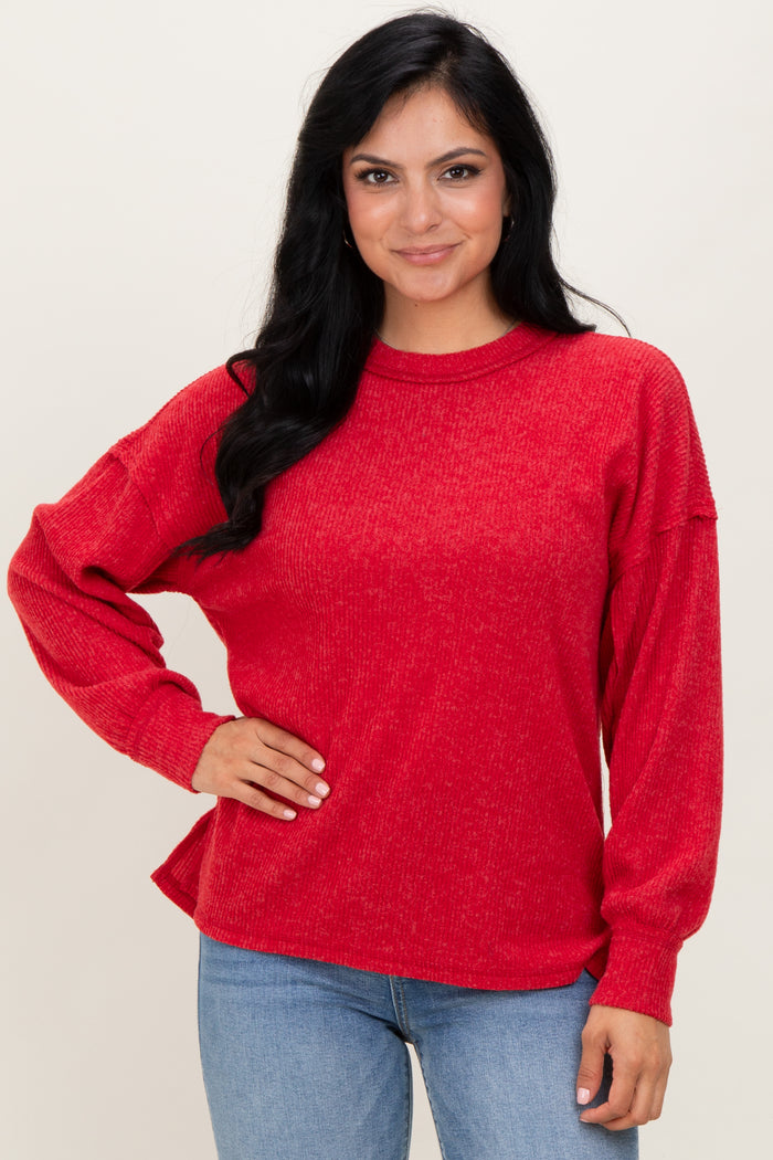 woman wearing a red relaxed fit long sleeve sweater with a textured fabric and side slits, paired with blue jeans