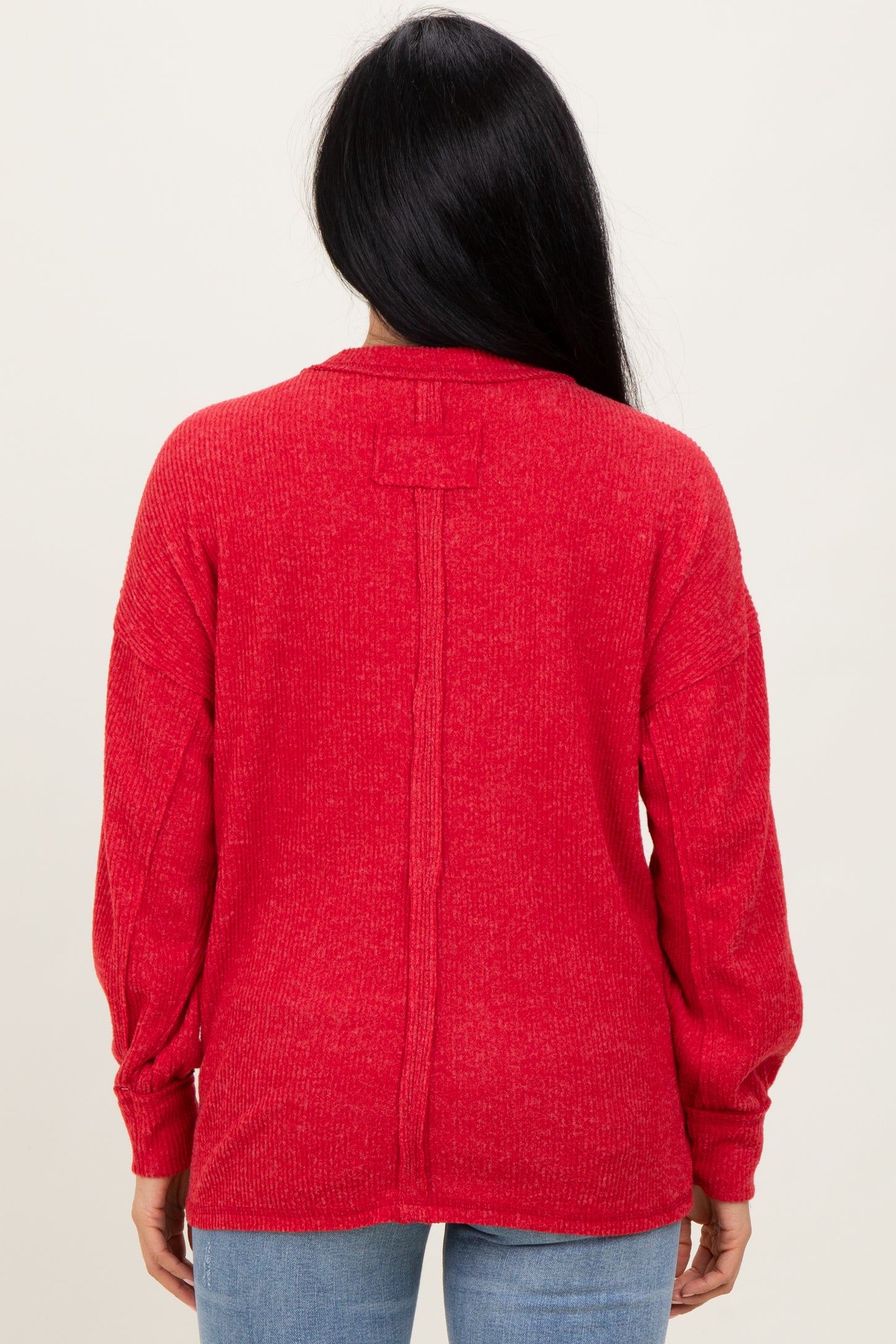 woman wearing a red long sleeve sweater with a relaxed fit and back seam detail, view from the back