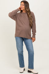 woman wearing a brown oversized maternity sweater with long sleeves and light blue straight leg jeans, showing her baby bump