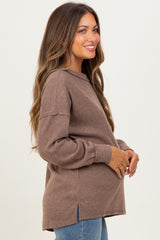 woman wearing a brown ribbed maternity sweater with side slits and holding her baby bump