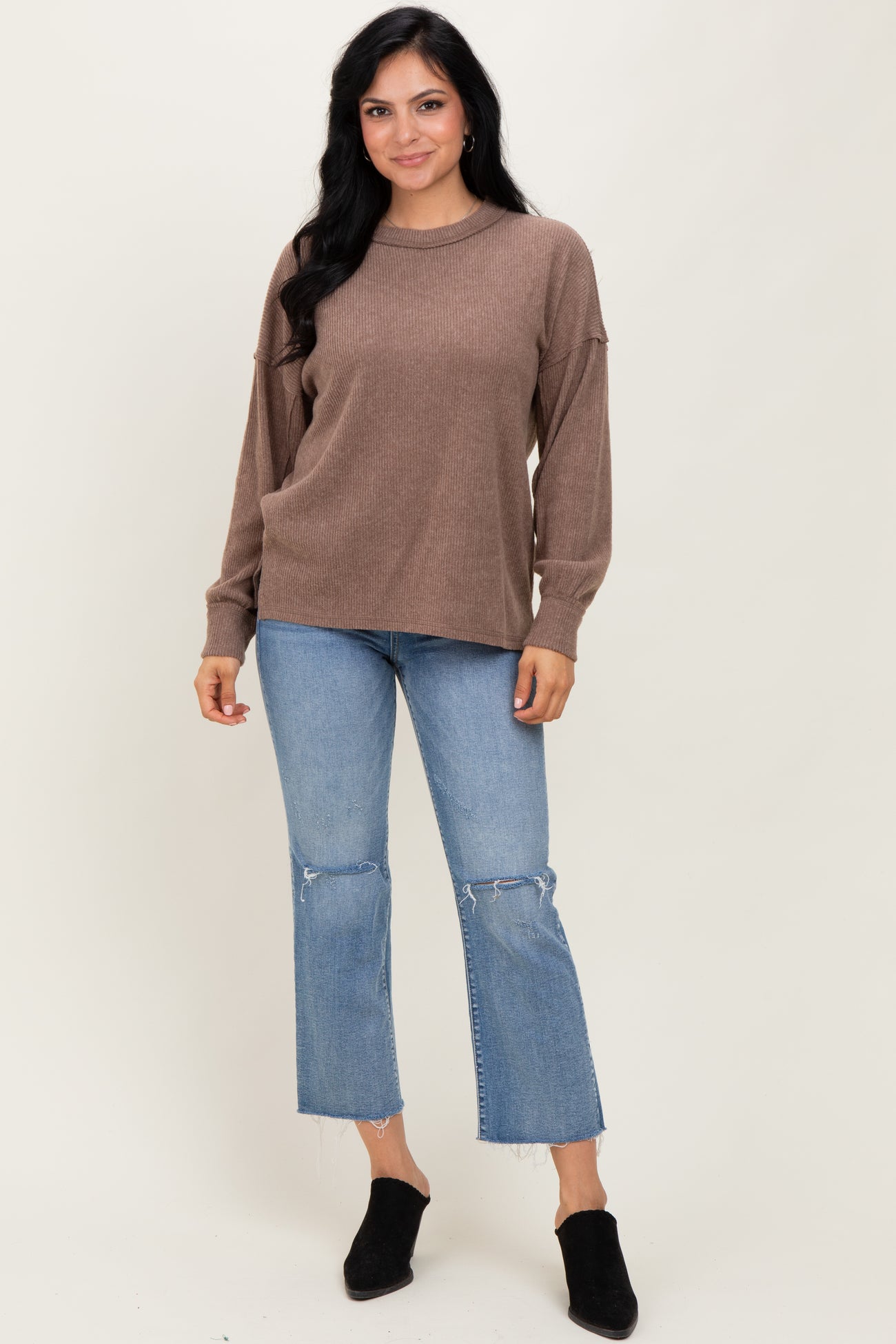 woman wearing a brown ribbed long sleeve sweater and light blue cropped jeans with a frayed hem