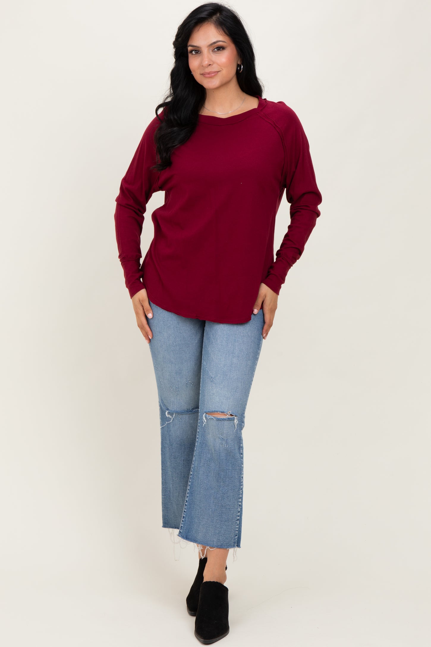 woman wearing a burgundy long sleeve top with a relaxed fit and light wash flare jeans