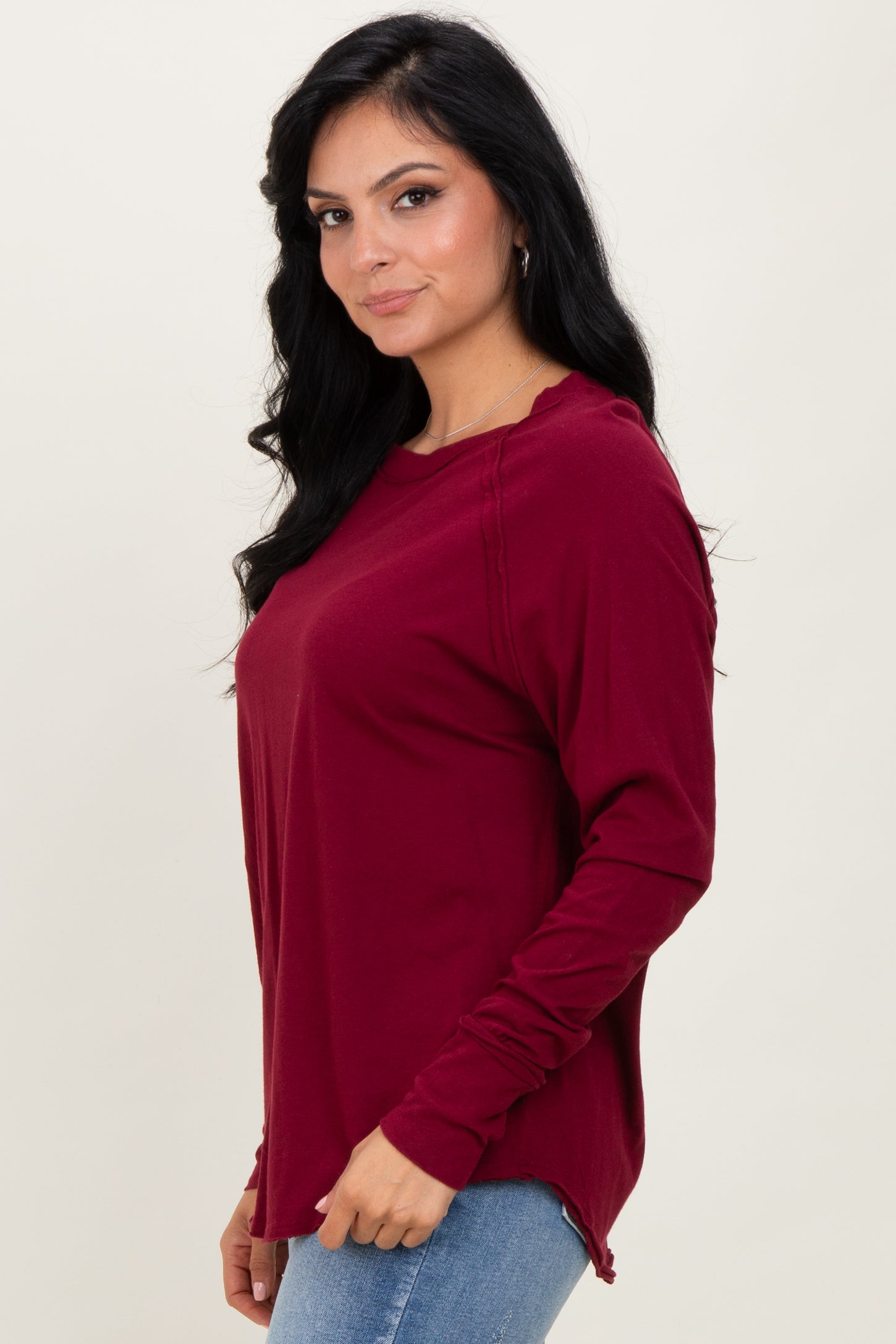 woman wearing a burgundy long sleeve top with side slits and a relaxed fit paired with blue jeans