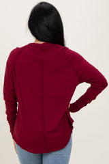 woman wearing a burgundy long sleeve top with a rounded hem and stitch detailing, view from the back