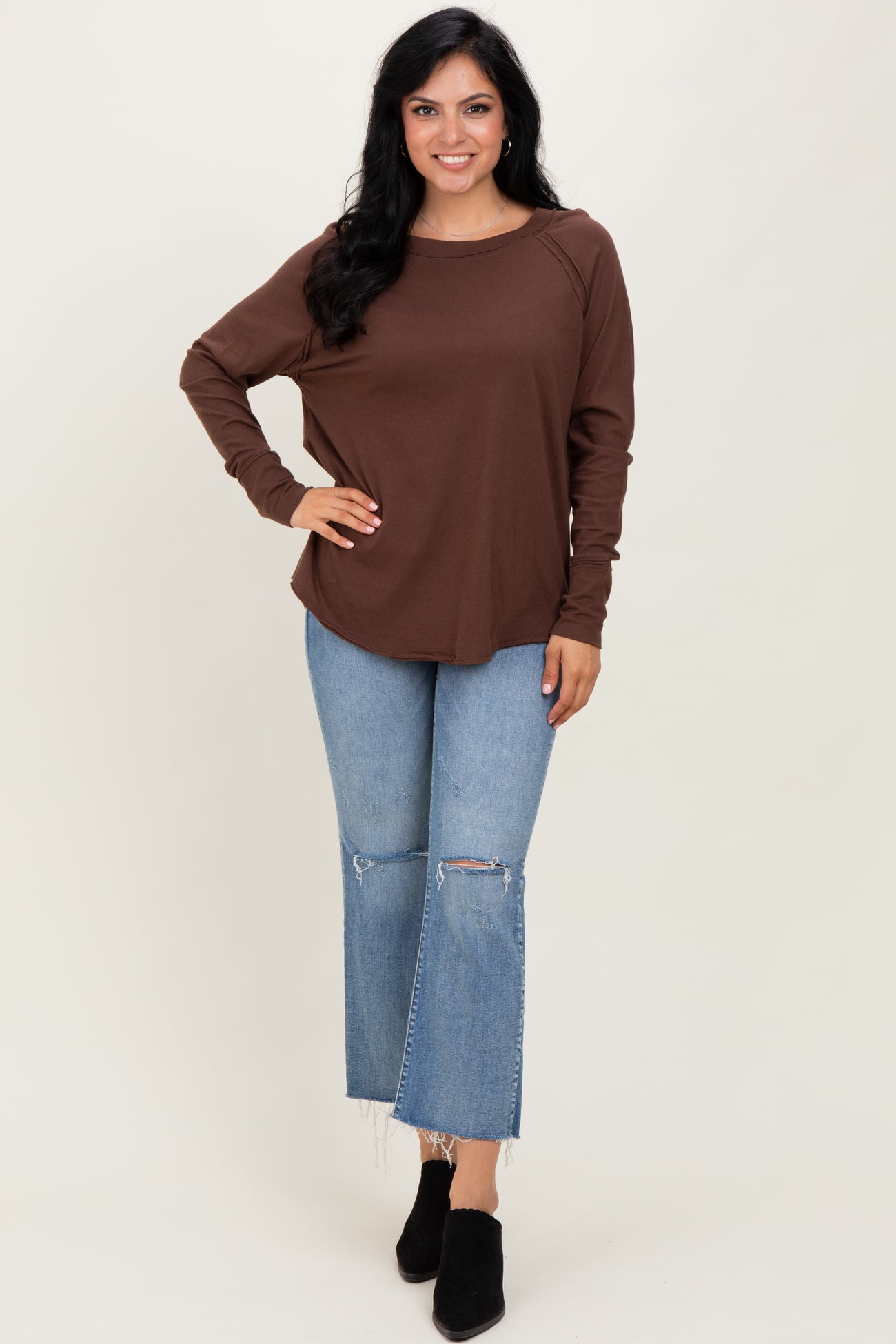woman wearing a brown long sleeve top with a relaxed fit and light blue distressed flare jeans