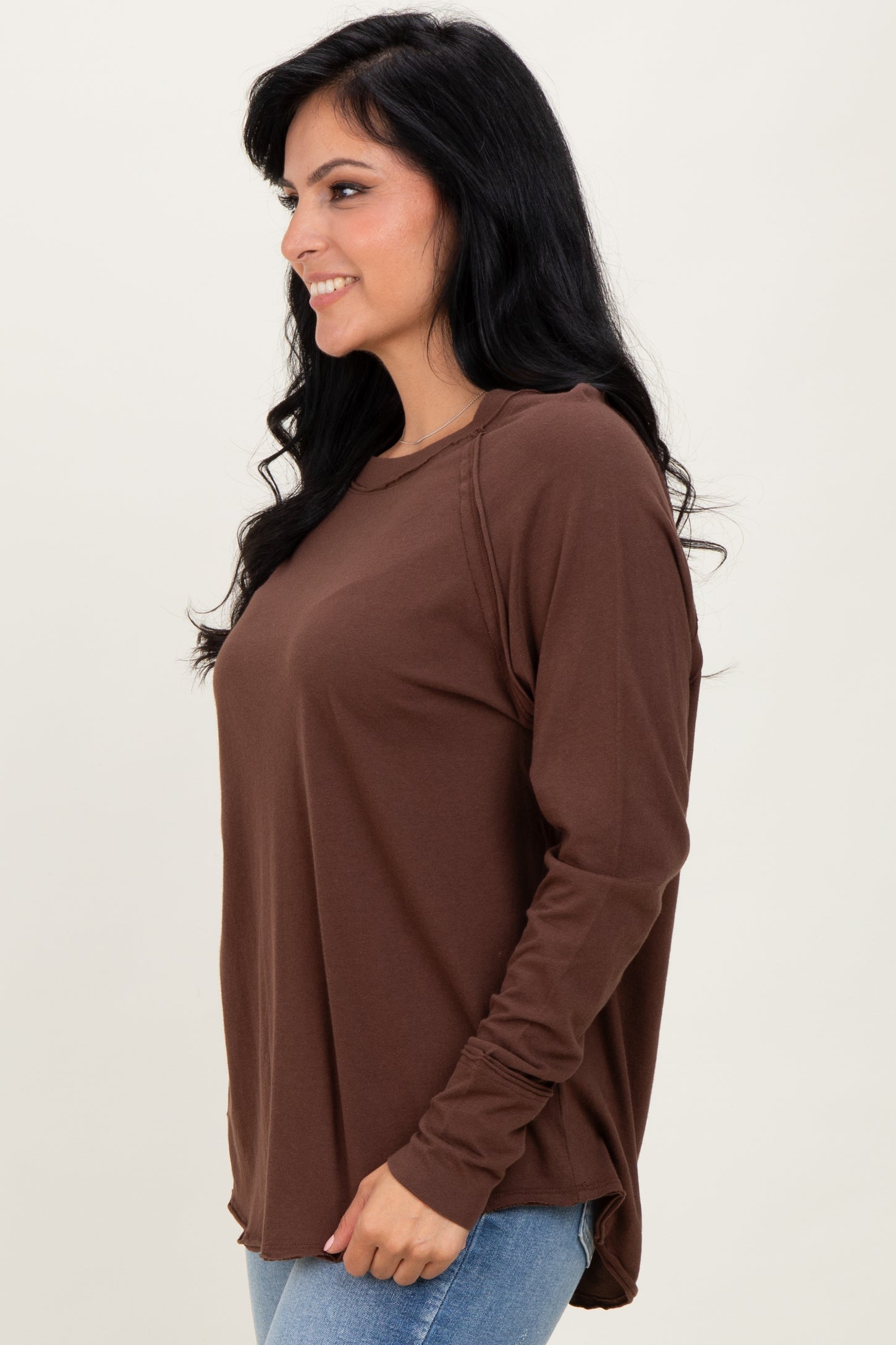 woman wearing a brown long sleeve top with a relaxed fit and side slits, styled with light blue jeans