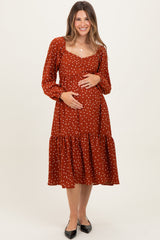woman wearing a rust polka dot maternity dress with a tiered hem and long sleeves, holding her baby bump