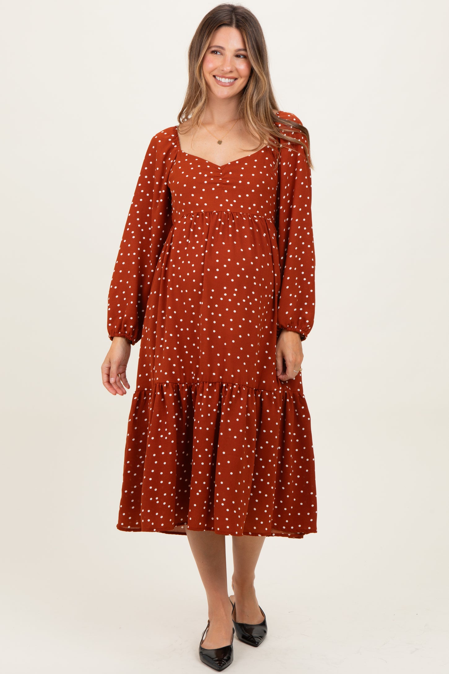 woman wearing a rust-colored polka dot maternity dress with long sleeves and a tiered skirt