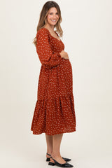 woman wearing a rust polka dot maternity dress with puff sleeves and tiered skirt, cradling her baby bump