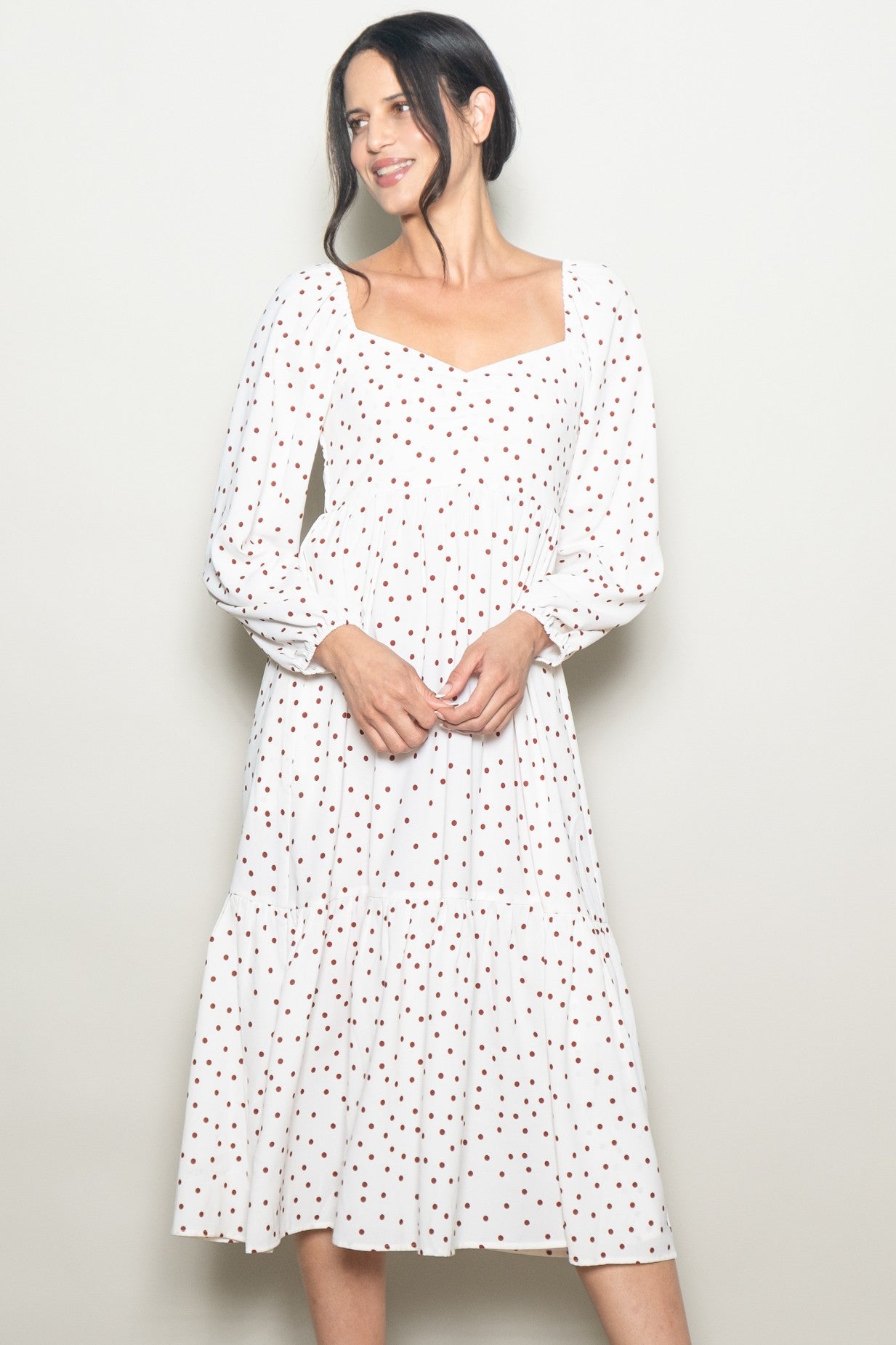 woman wearing a white midi dress with red polka dots and long puff sleeves, smiling against a light background