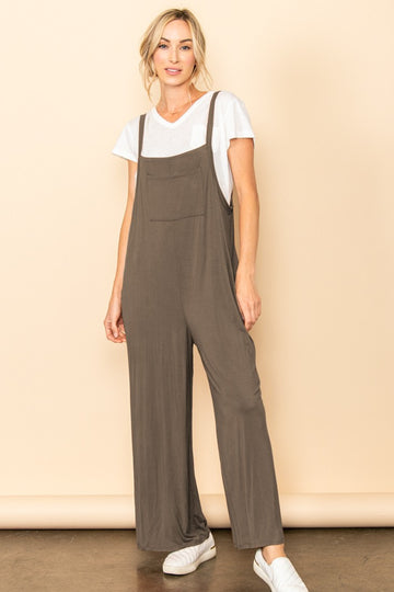 woman wearing a brown sleeveless jumpsuit over a white t-shirt with a front pocket and white sneakers