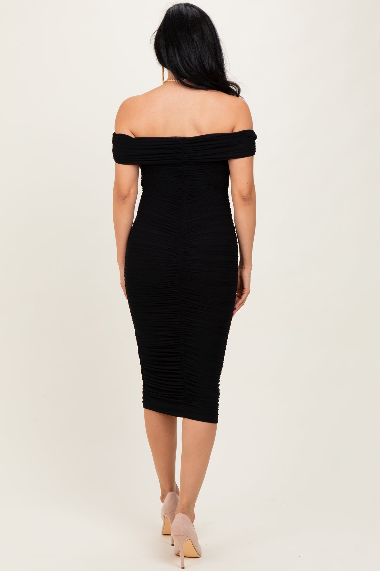 woman wearing a black off-the-shoulder bodycon dress with ruched detailing and a form-fitting silhouette