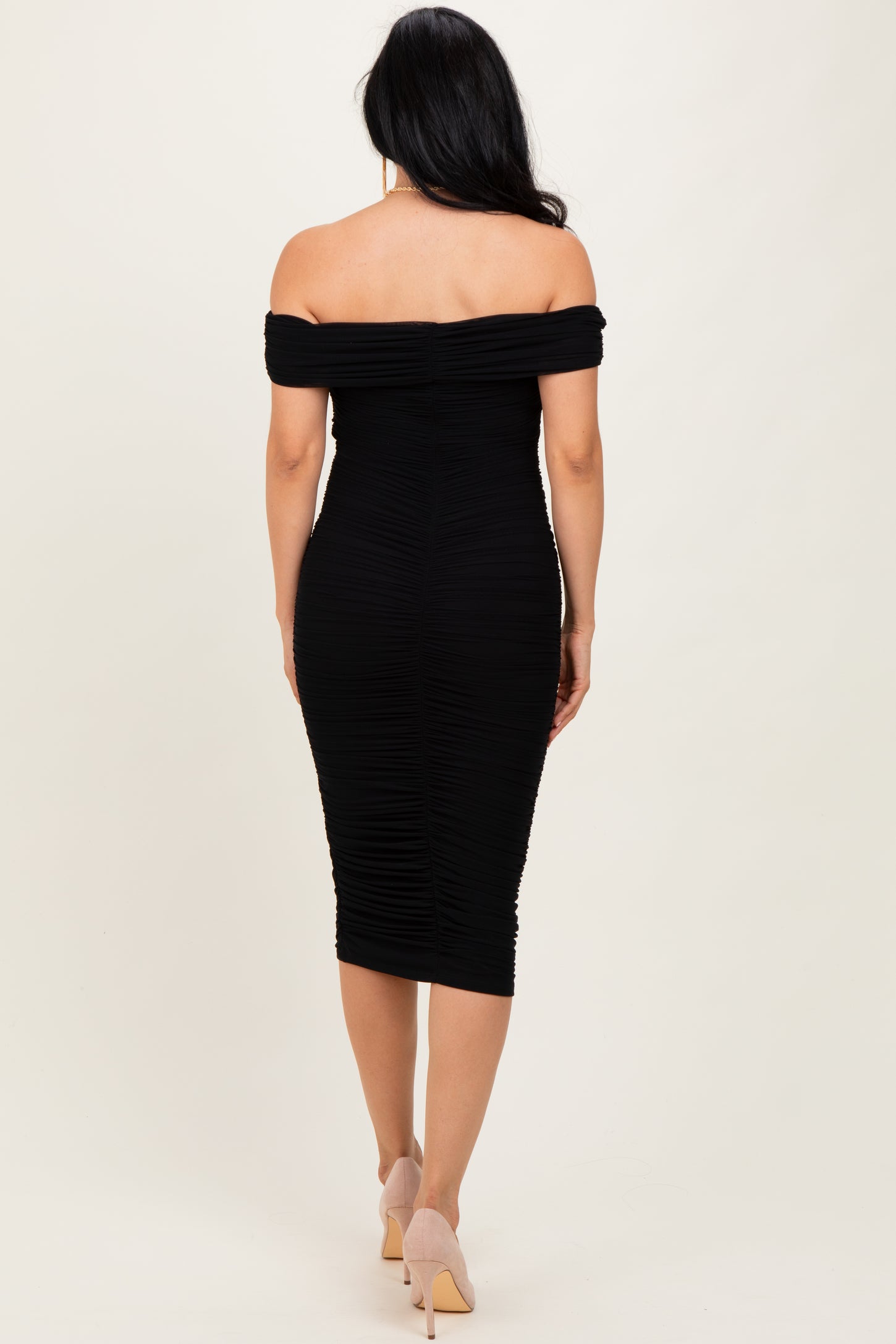 woman wearing a black off-the-shoulder bodycon dress with ruched detailing and a form-fitting silhouette