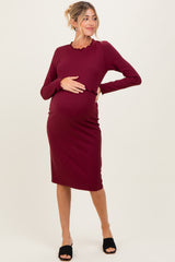 woman wearing a burgundy ribbed maternity dress with long sleeves and a scalloped neckline, showing her baby bump