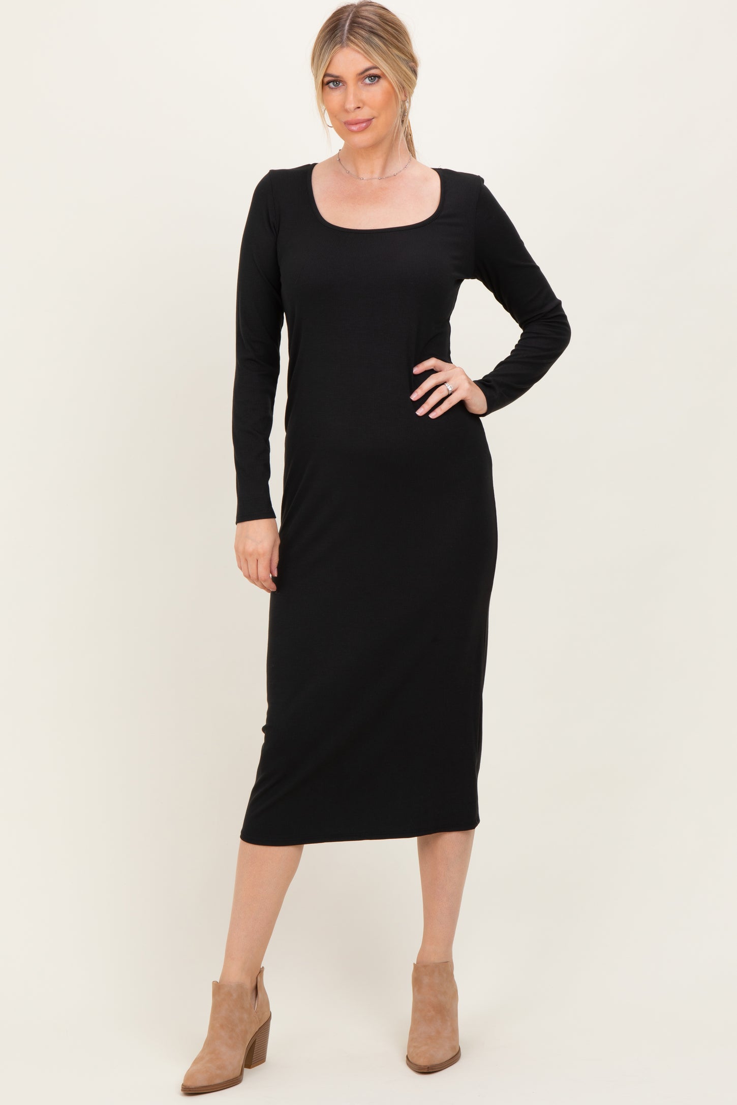 woman wearing a black long sleeve midi dress with a scoop neckline and tan heeled boots