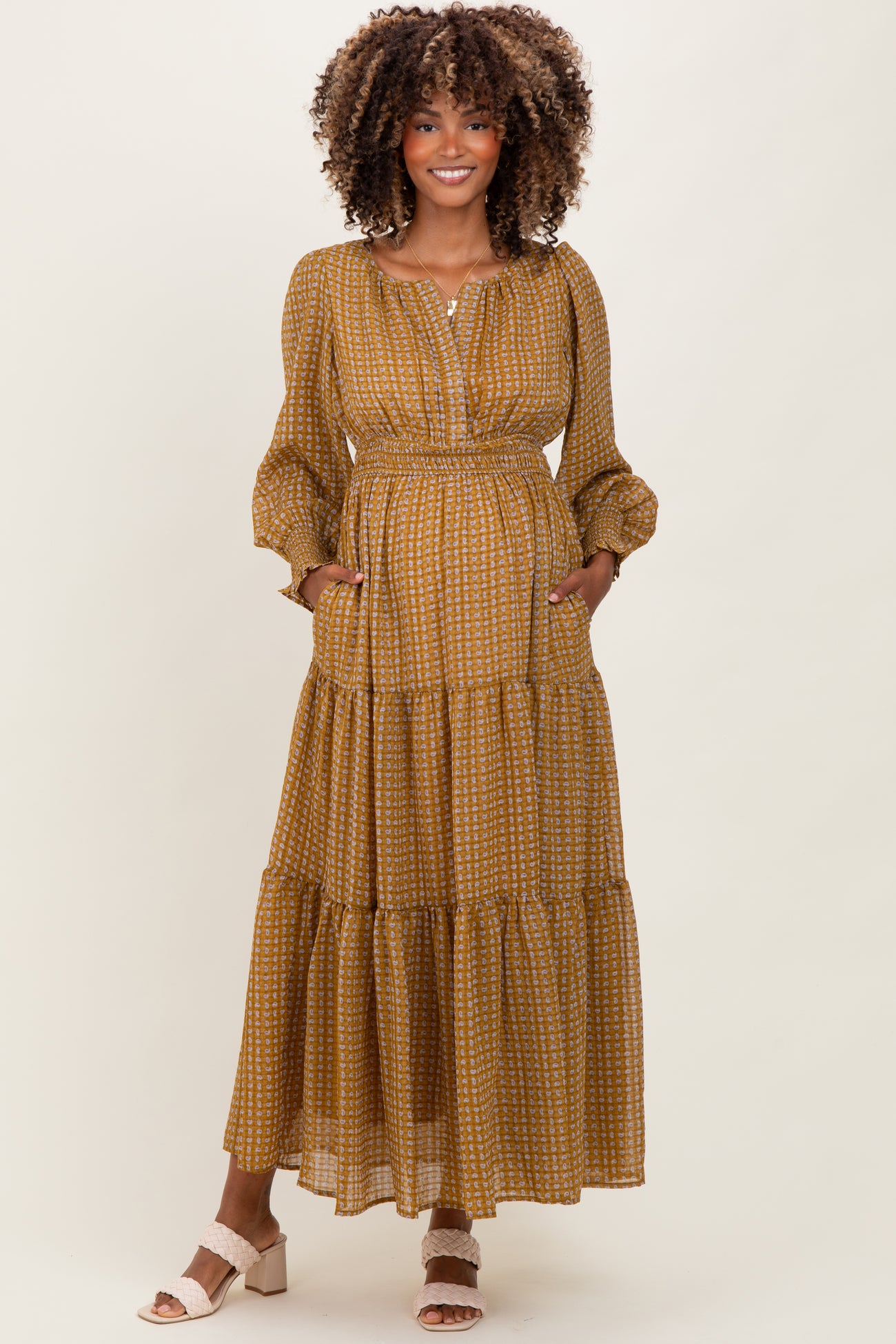 woman wearing a mustard yellow patterned maternity maxi dress with long sleeves and pockets, showcasing her baby bump