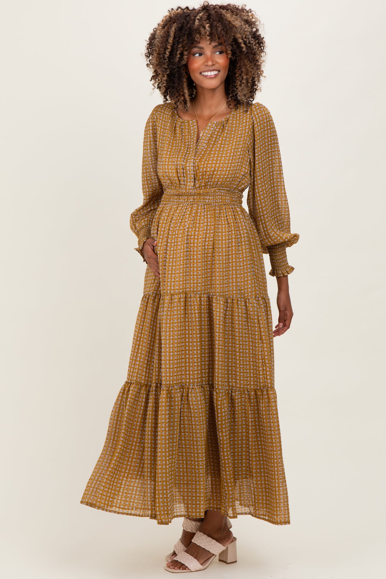 woman wearing a mustard patterned long sleeve maternity dress with an elastic waistband and tiered skirt, showing her baby bump
