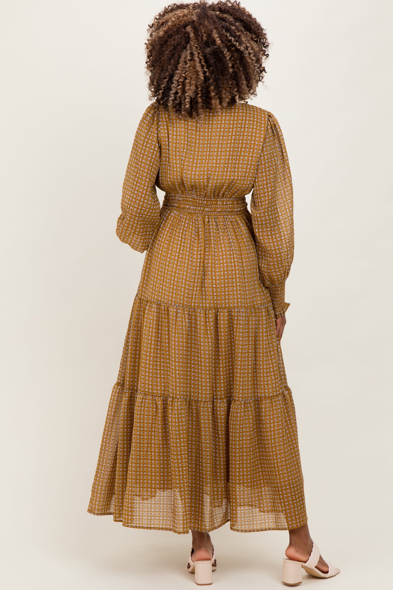woman wearing a mustard yellow tiered maternity dress with long sleeves and a fitted waist from the back