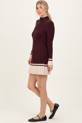 woman wearing a burgundy ribbed long sleeve sweater dress with a pleated beige hem and black flats