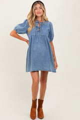 woman wearing a light denim maternity dress with puff sleeves and a tie neckline, showcasing her baby bump