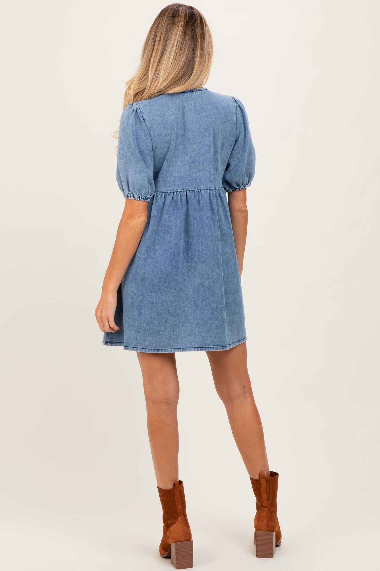 woman wearing a light blue denim puff sleeve maternity dress, showing a relaxed fit and gathered waist detail