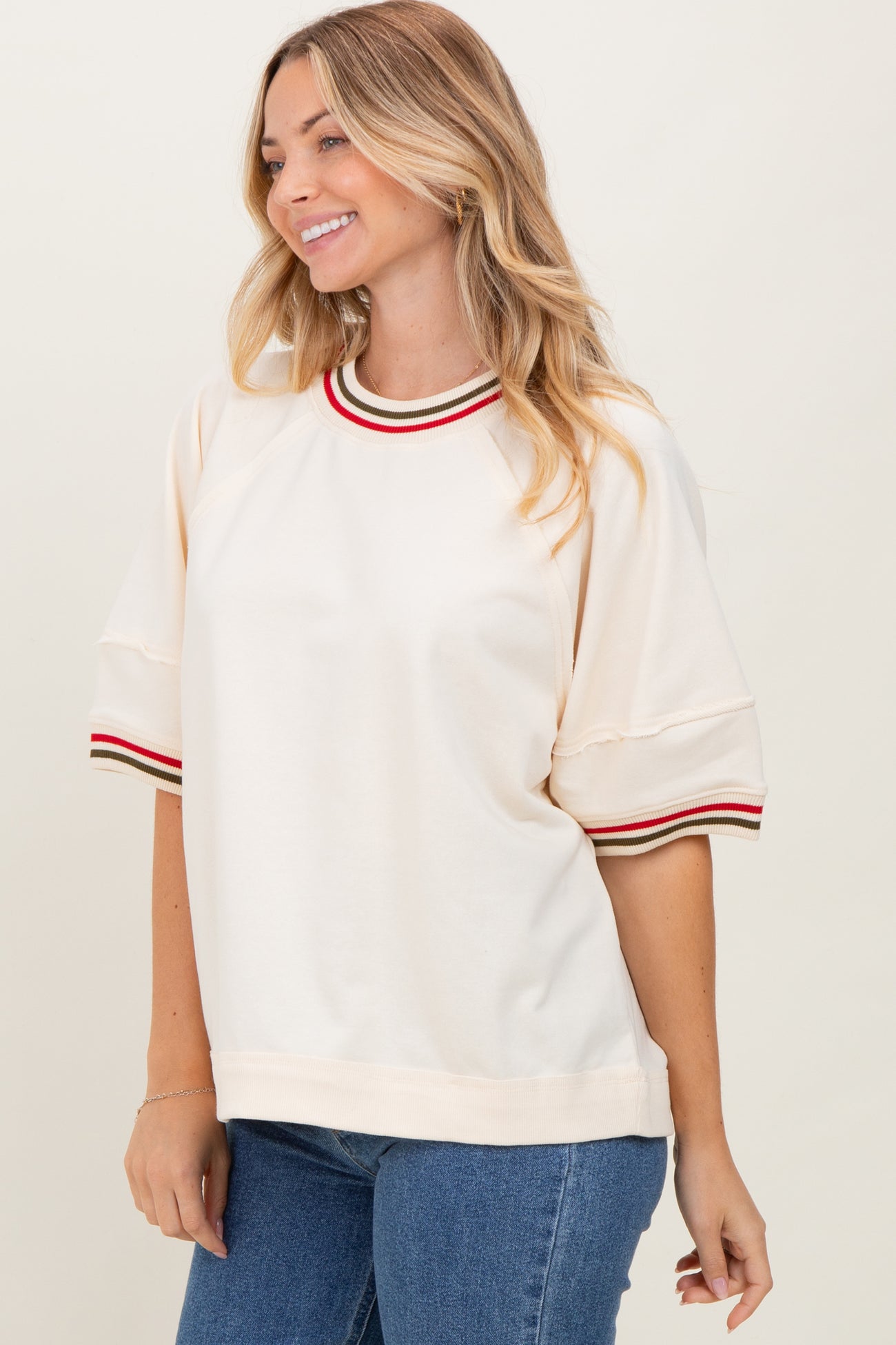 woman wearing a cream short sleeve sweatshirt with red and green striped neckline and sleeve details