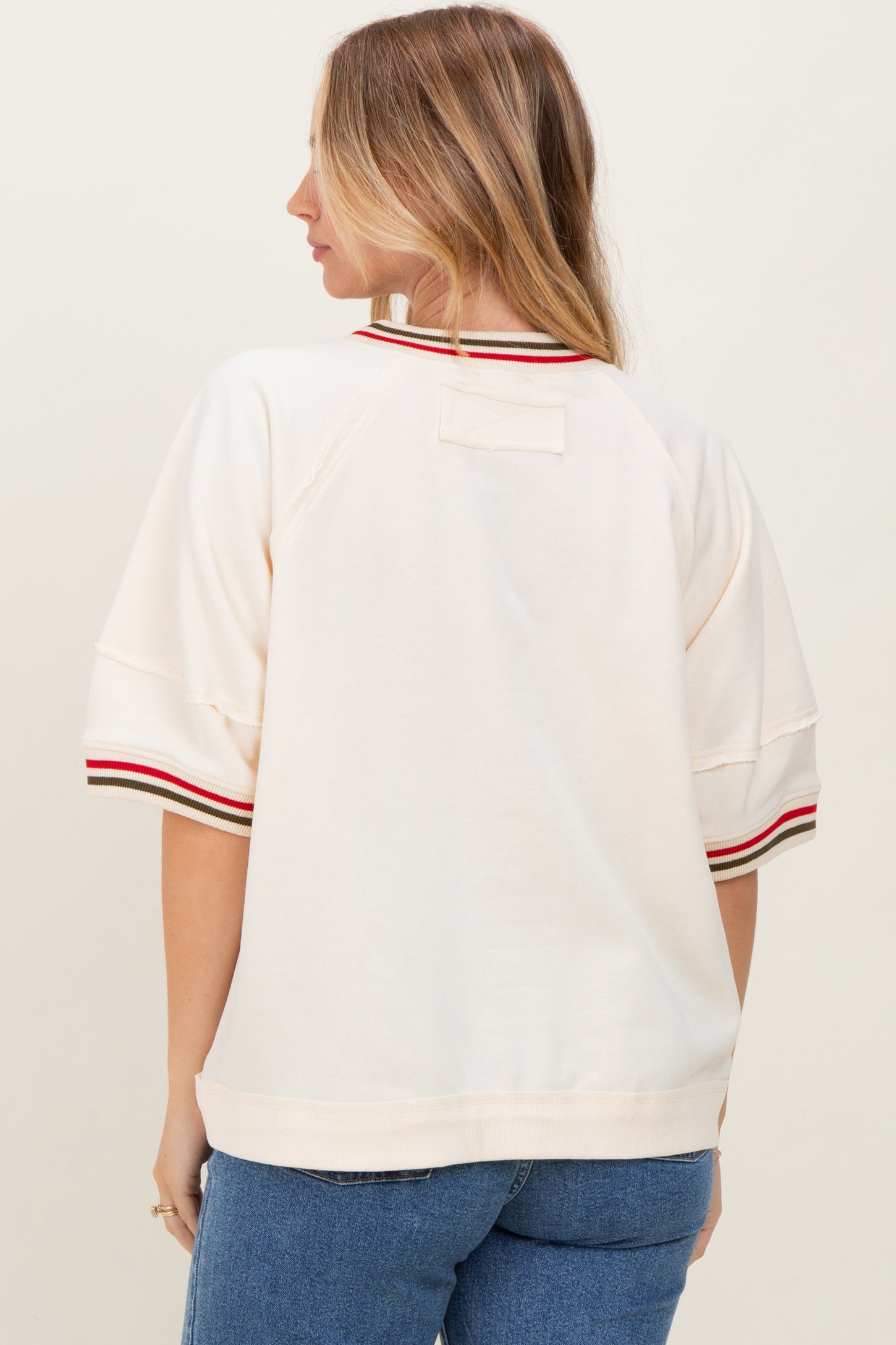 woman wearing a cream oversized sweatshirt with red and green striped details on the sleeves