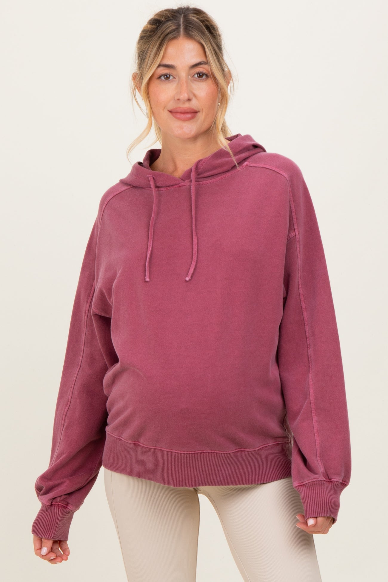 woman wearing a maroon maternity hoodie with a relaxed fit and hoodie strings, showcasing a visible baby bump