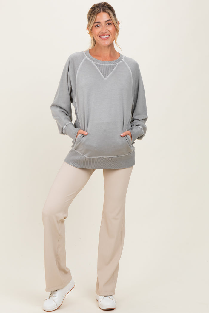 woman wearing a grey maternity sweatshirt with pockets and beige maternity pants, standing casually