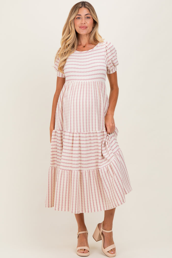 woman wearing a pink and white striped maternity dress with short sleeves and a tiered skirt, holding her baby bump