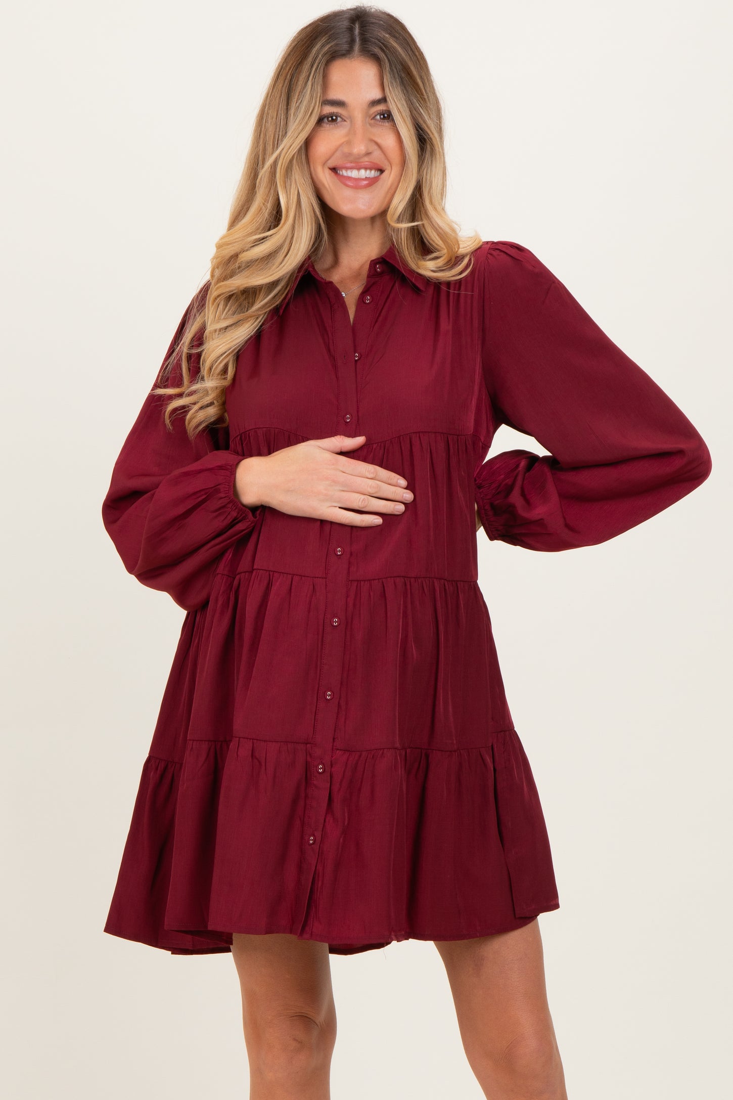 woman wearing a burgundy maternity dress with puff sleeves and tiered design, holding her baby bump