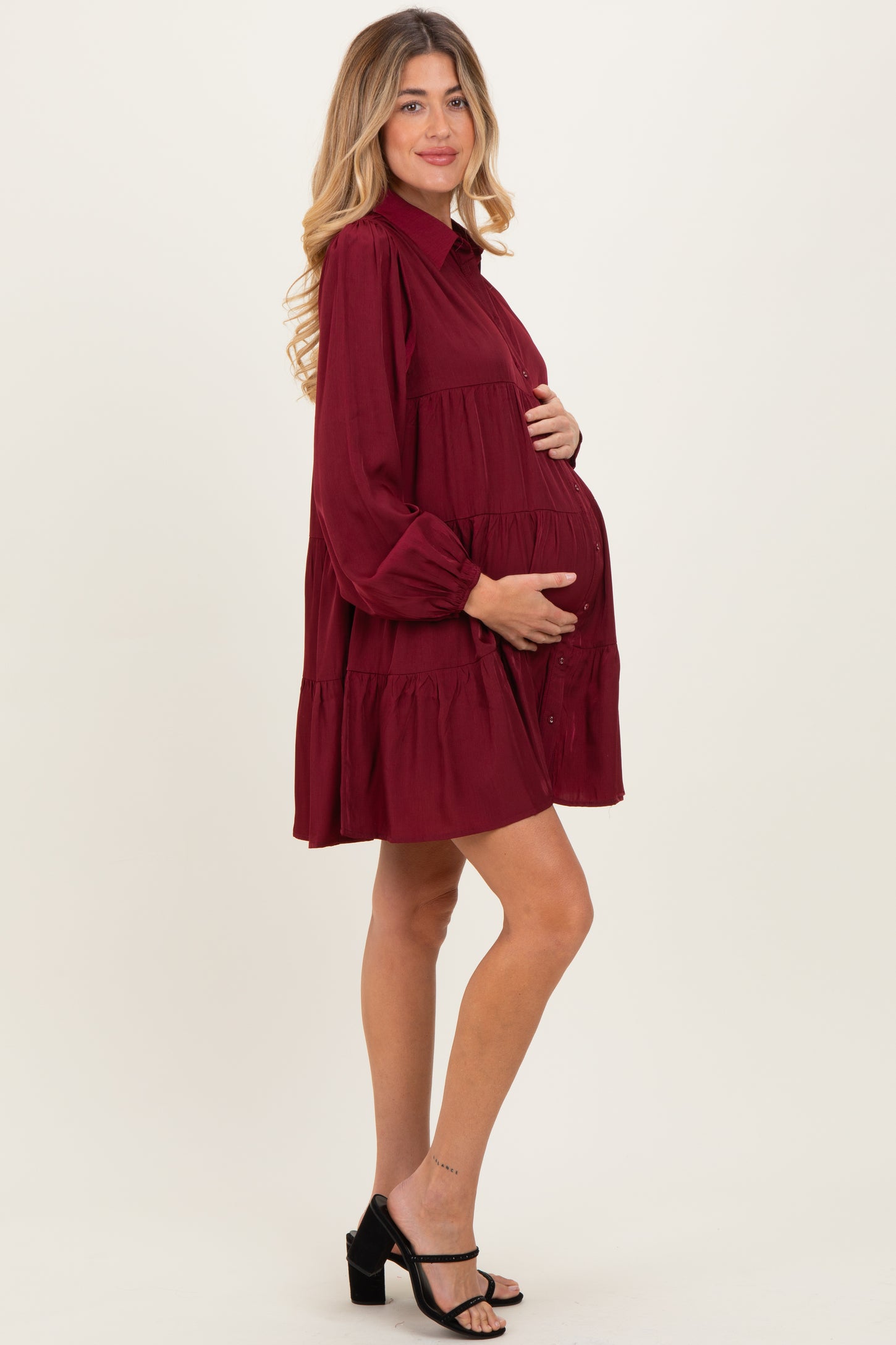woman wearing a burgundy maternity dress with long sleeves and tiered skirt, holding her baby bump