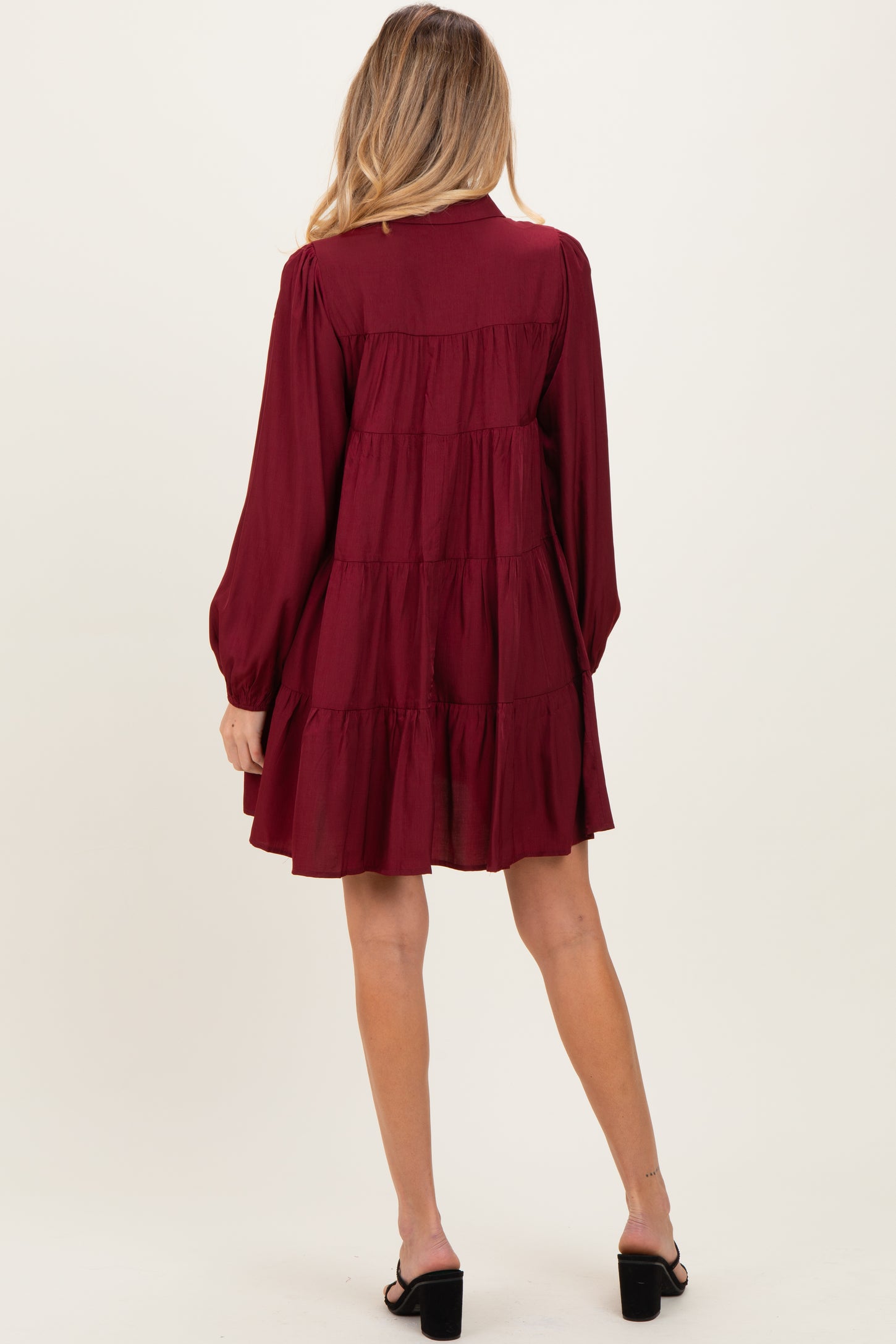 woman wearing a burgundy maternity dress with long sleeves and tiered ruffles, showing a flowing silhouette from the back