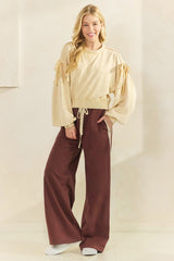 woman wearing a beige cropped sweatshirt with tie sleeves and brown wide-leg pants