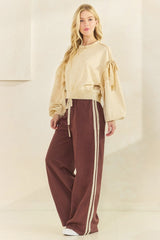 woman wearing a cream oversized sweatshirt with puff sleeves and brown sweatpants featuring side stripes