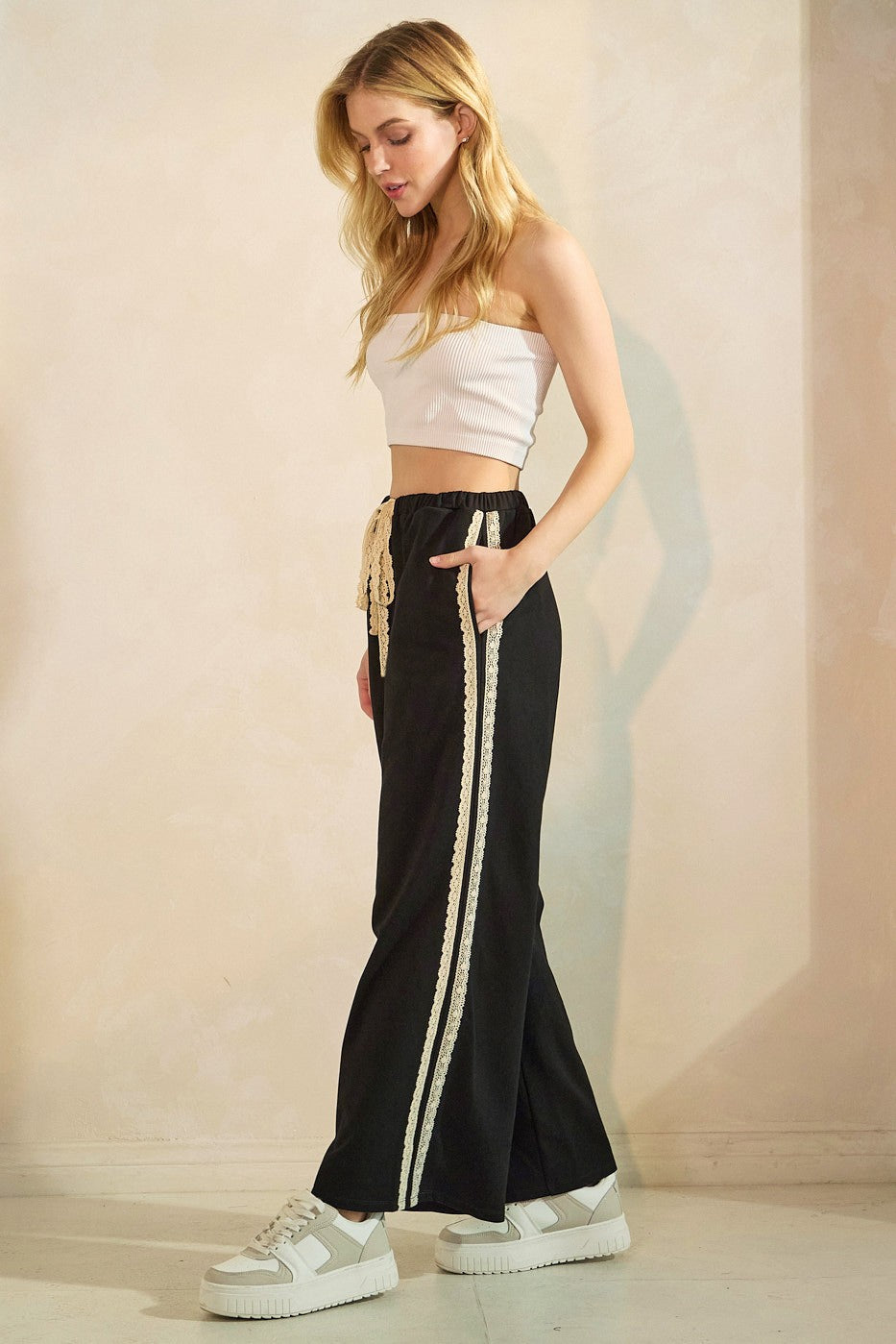 woman wearing a black wide-leg pant with lace side details and a white cropped top, paired with white sneakers