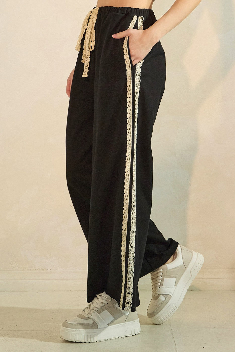 woman wearing black wide-leg pants with lace trim and drawstring waist, paired with white sneakers