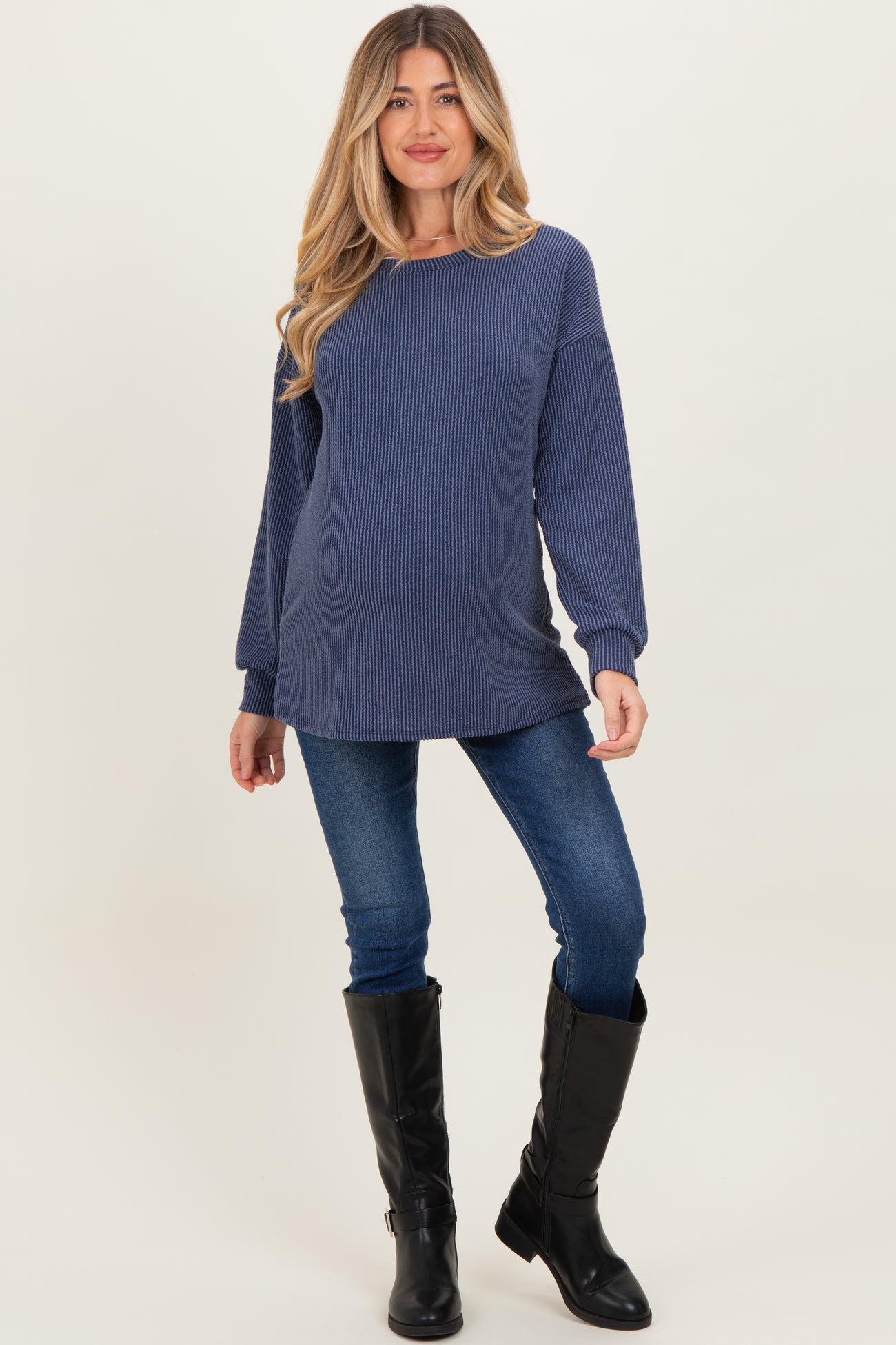 woman wearing a navy striped maternity sweater with long sleeves and paired with blue skinny jeans and black knee-high boots